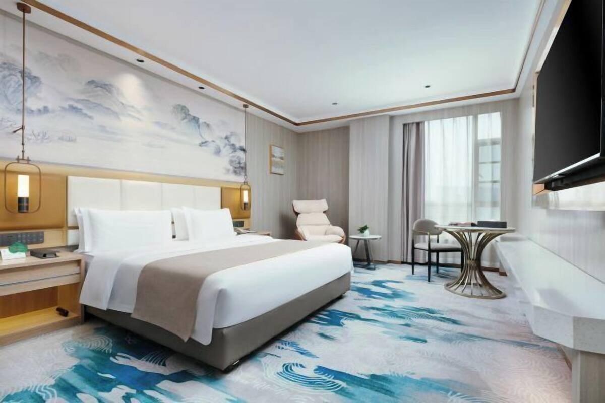 Una habitación de hotel con una cama grande, televisión, escritorio con silla y una mesita.