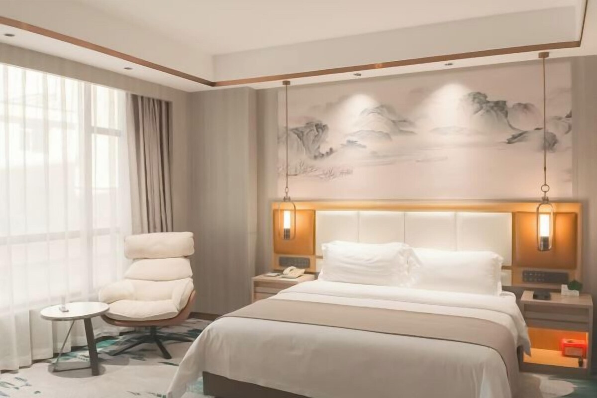 Una habitación de hotel con una cama grande, una silla, una mesita de noche y una pared decorada con obras de arte.