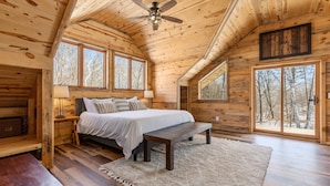Une chambre dans une cabane en bois, avec un lit, un banc et de grandes fenêtres.