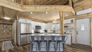 Une cuisine moderne dotée d’un îlot central, de meubles blancs, d’appareils électroménagers en acier inoxydable et d’un plafond en bois.