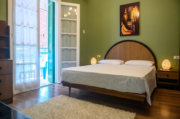 A bedroom with a bed, a nightstand, a wall-mounted lamp, and a door leading to an outdoor area.