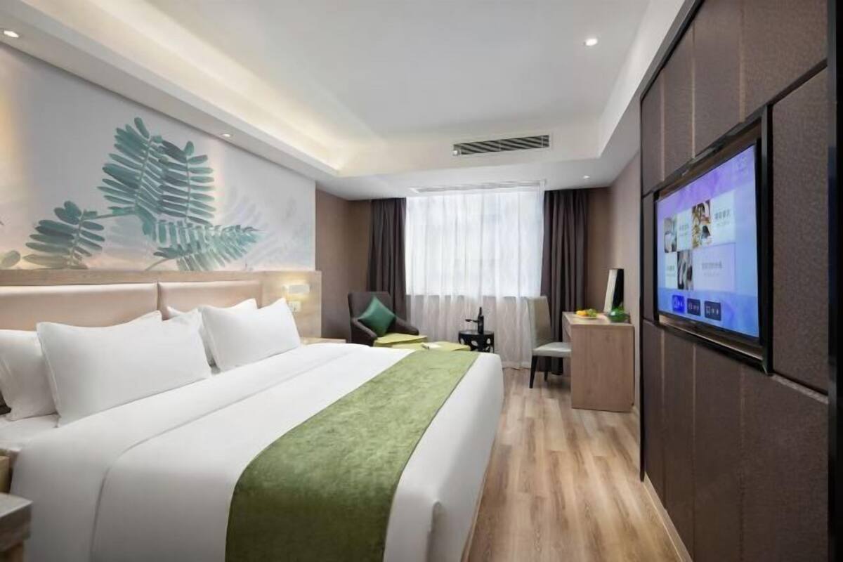 Een hotelkamer met een bed, bureau, stoel, televisie en een groot raam met gordijnen.
