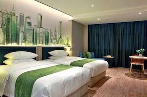 Habitación de hotel con dos camas, un mural con vista a la ciudad, una mesita con una planta y una cortina azul.