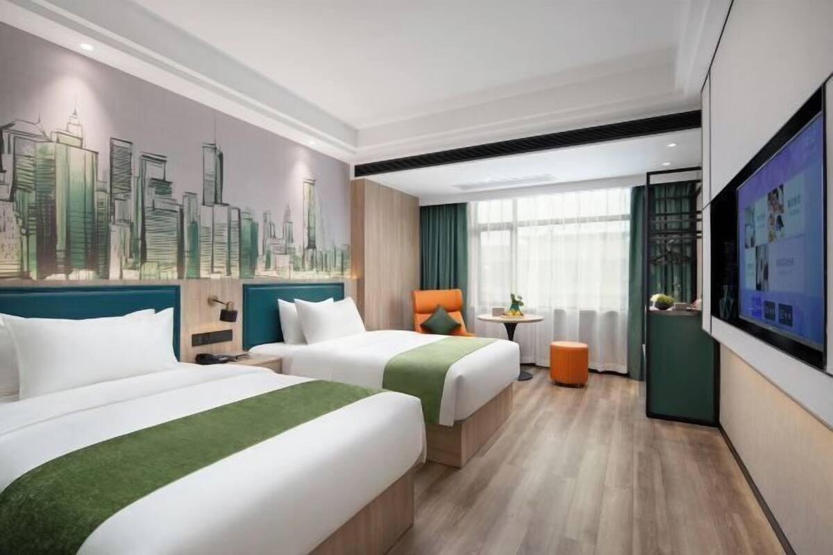 Een hotelkamer met twee bedden, een stadslandschap muurschildering, een televisie en een raam met gordijnen.