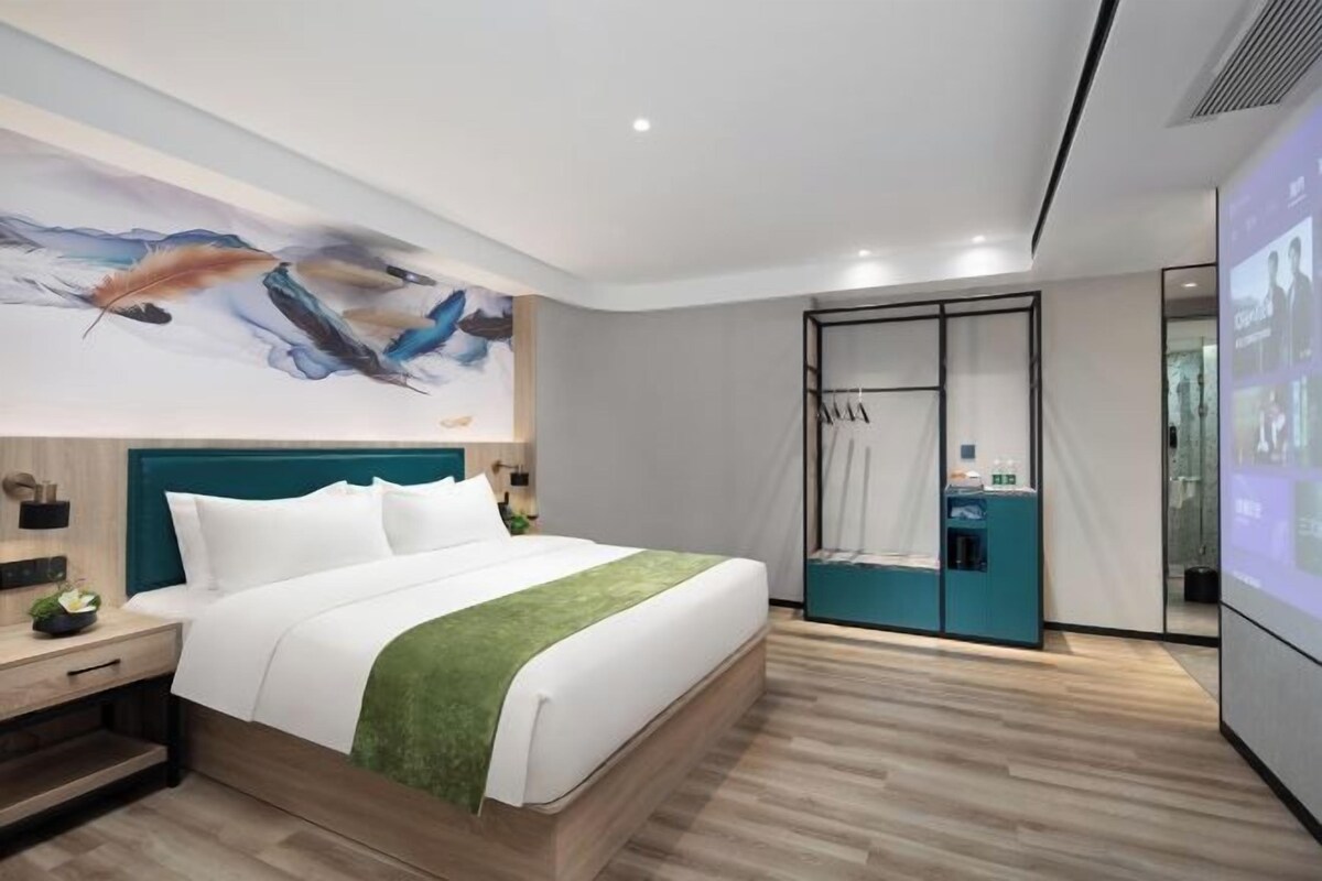 A modern hotel room with a bed, a green throw, a painting on the wall, and a sliding door closet.