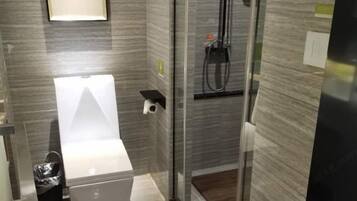 Un baño moderno con cabina de ducha de vidrio, inodoro y una pequeña repisa.