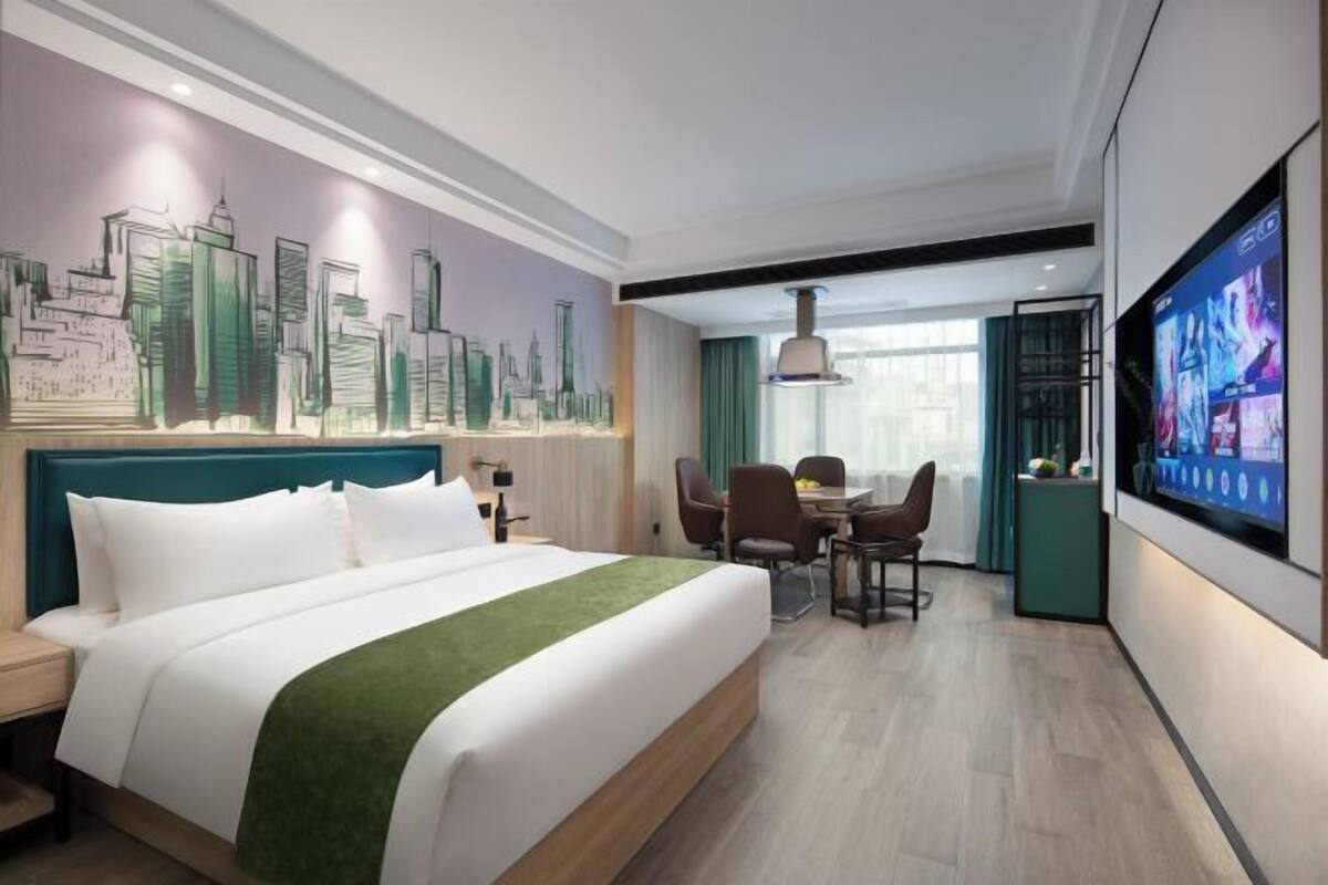 Een hotelkamer met een groot bed, een zithoek met stoelen en een tafel, een aan de muur bevestigde televisie en een stadslandschap op de muur.