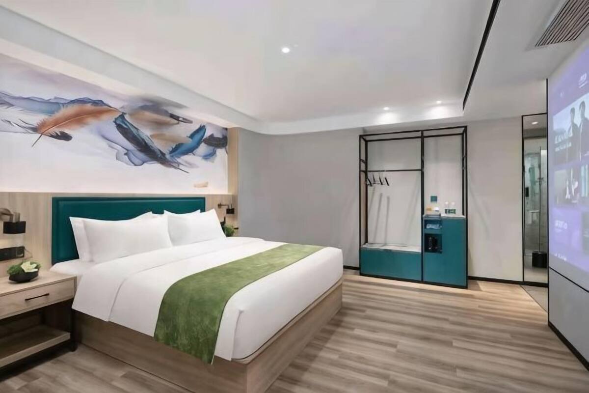 Een moderne hotelkamer met een groot bed, een groene plaid, een tv aan de muur en een badkamer met een glazen deur.