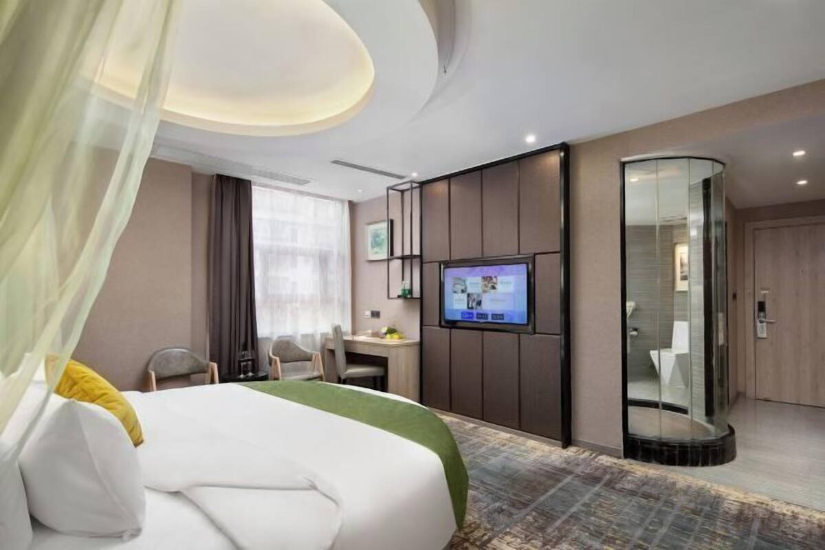 Een hotelkamer met een bed, een bureau, een televisie en een douchecabine met glazen wanden.