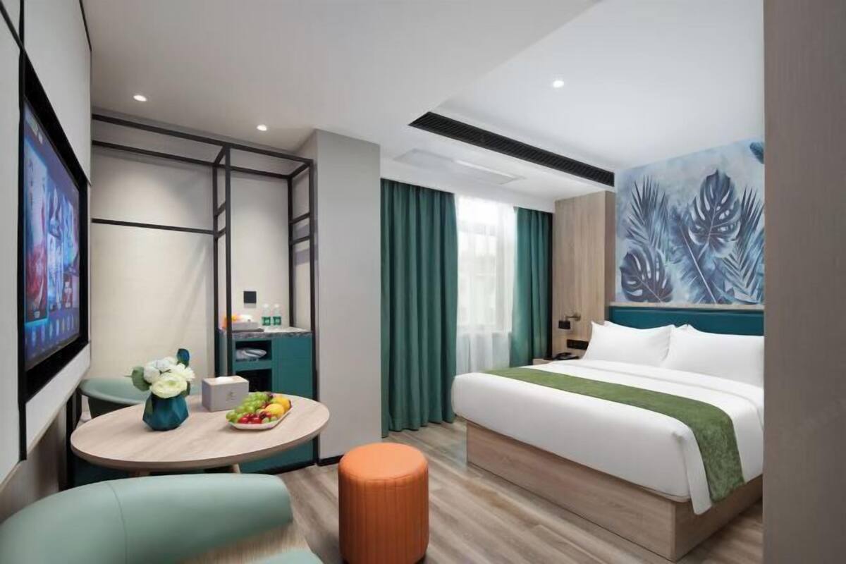 Een moderne hotelkamer met een bed, een bureau, een stoel, een klein tafeltje met fruit en een schilderij aan de muur.