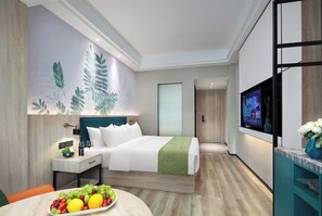A modern hotel room with a bed, bedside table, TV, and a fruit bowl.