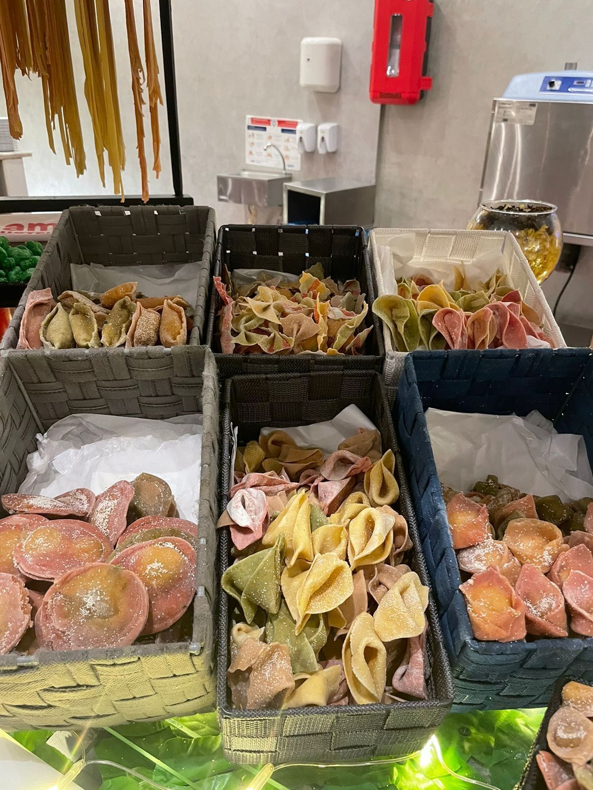 A display of various pasta types in baskets, with a kitchen area in the background.