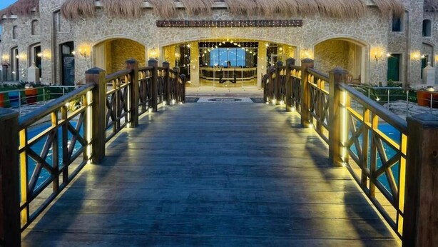 Un edificio de piedra con tejado de paja, una terraza de madera que conduce a la entrada principal, y vista al mar.