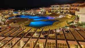 Un complejo turístico con varias edificaciones, una zona de piscina central y una estructura de techo de paja.