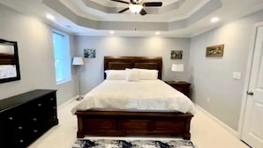 A bedroom with a large bed, a ceiling fan, a nightstand, a lamp, and artwork on the walls. - Relaxing Stay on Trade Street (Greer)