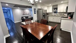 A modern kitchen with white cabinets, a stainless steel refrigerator, and a dining area with a wooden table and chairs. - Relaxing Stay on Trade Street (Greer)