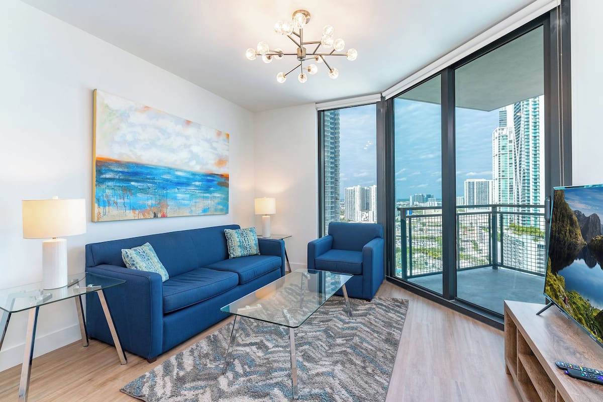 A modern living room with a blue sofa, a glass coffee table, and a large TV on a wooden stand.