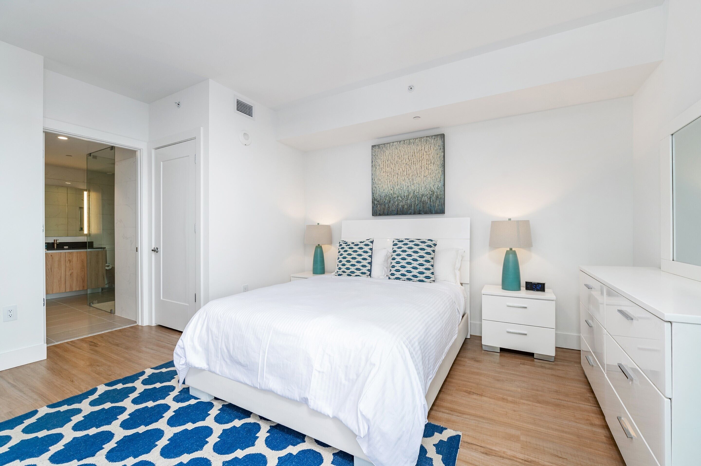 A modern bedroom with a large bed, white nightstands, a bedside table, and a wardrobe.