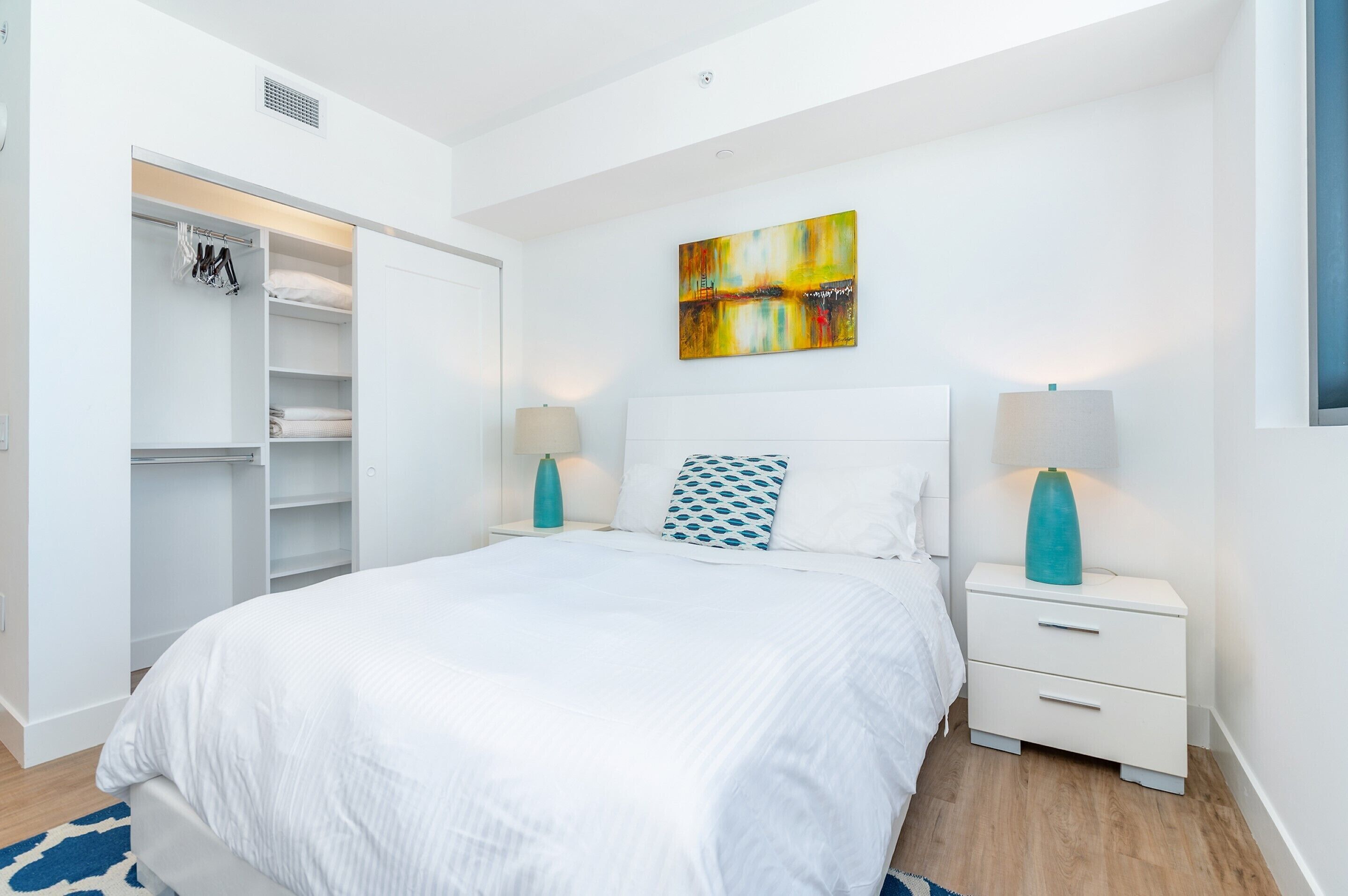 Un dormitorio con cama, mesitas de noche, un armario y un cuadro en la pared.