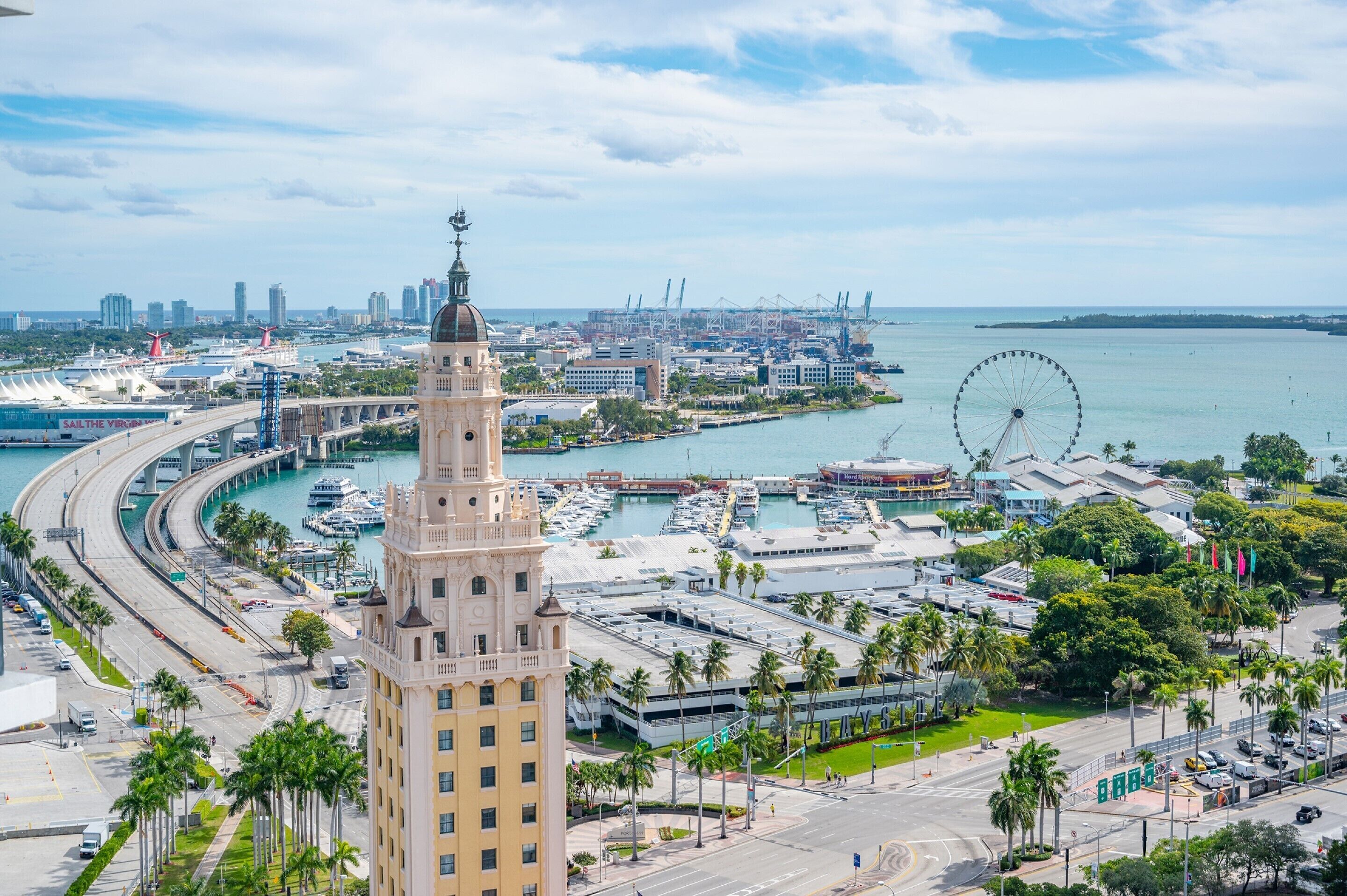 A coastal cityscape with a prominent tower, marina, and a large Ferris wheel.