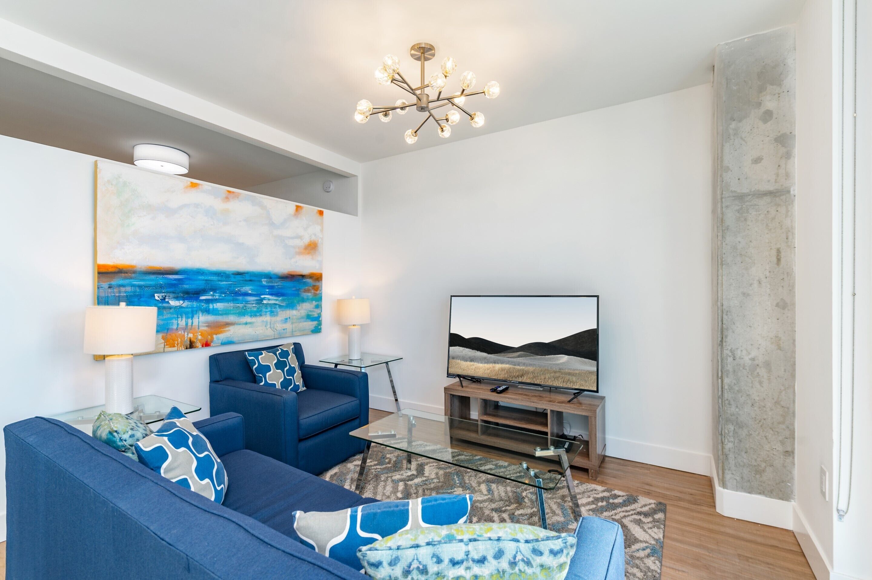 Un soggiorno moderno con un divano blu, un tavolino in vetro, una TV a schermo piatto e un grande quadro astratto appeso al muro.