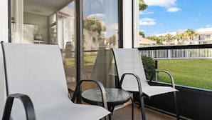 Ein Balkon mit zwei Stühlen und einem kleinen Tisch, der auf eine Wiese und einen weißen Zaun blickt.