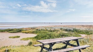 A beach with a wooden picnic table in the foreground and a clear sky.