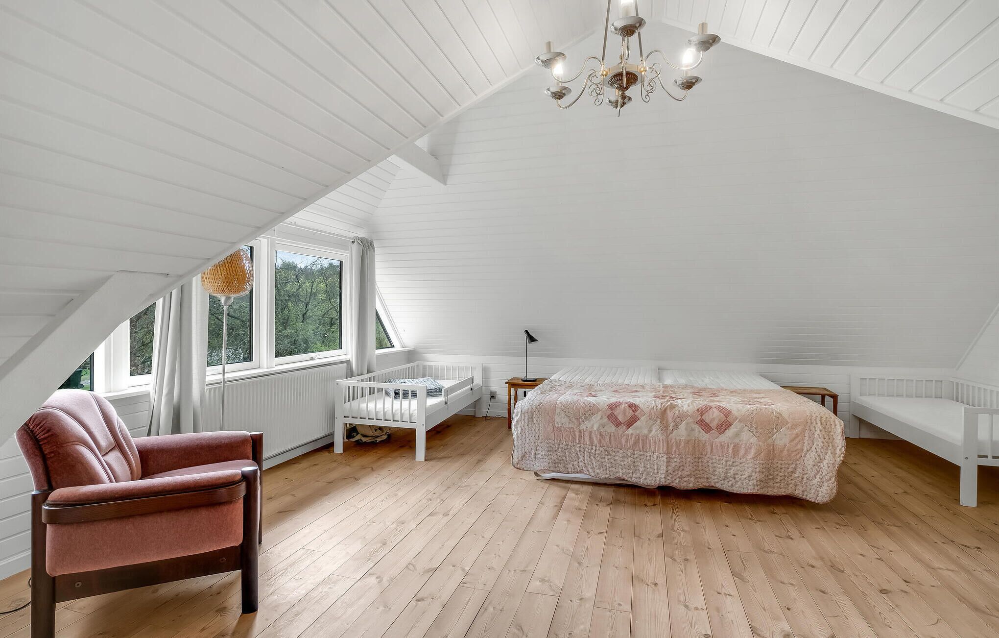 Un dormitorio con techo inclinado, una cama, una silla y una ventana con vistas a árboles.