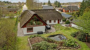 A traditional house with a thatched roof, a small garden with a pond, and a view of the surrounding village.
