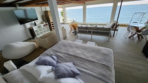 A modern bedroom with a large bed, a TV, a wooden cabinet, and a view of the sea. - HOTEL BOUTIQUE ATENAS  (Paracas)