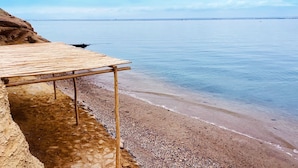 A wooden bench on a pebbled beach with a clear view of the water and distant shoreline. - HOTEL BOUTIQUE ATENAS  (Paracas)