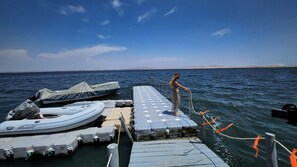 A dock with a person standing on it, a covered boat, and a row of inflatable boats. - HOTEL BOUTIQUE ATENAS  (Paracas)