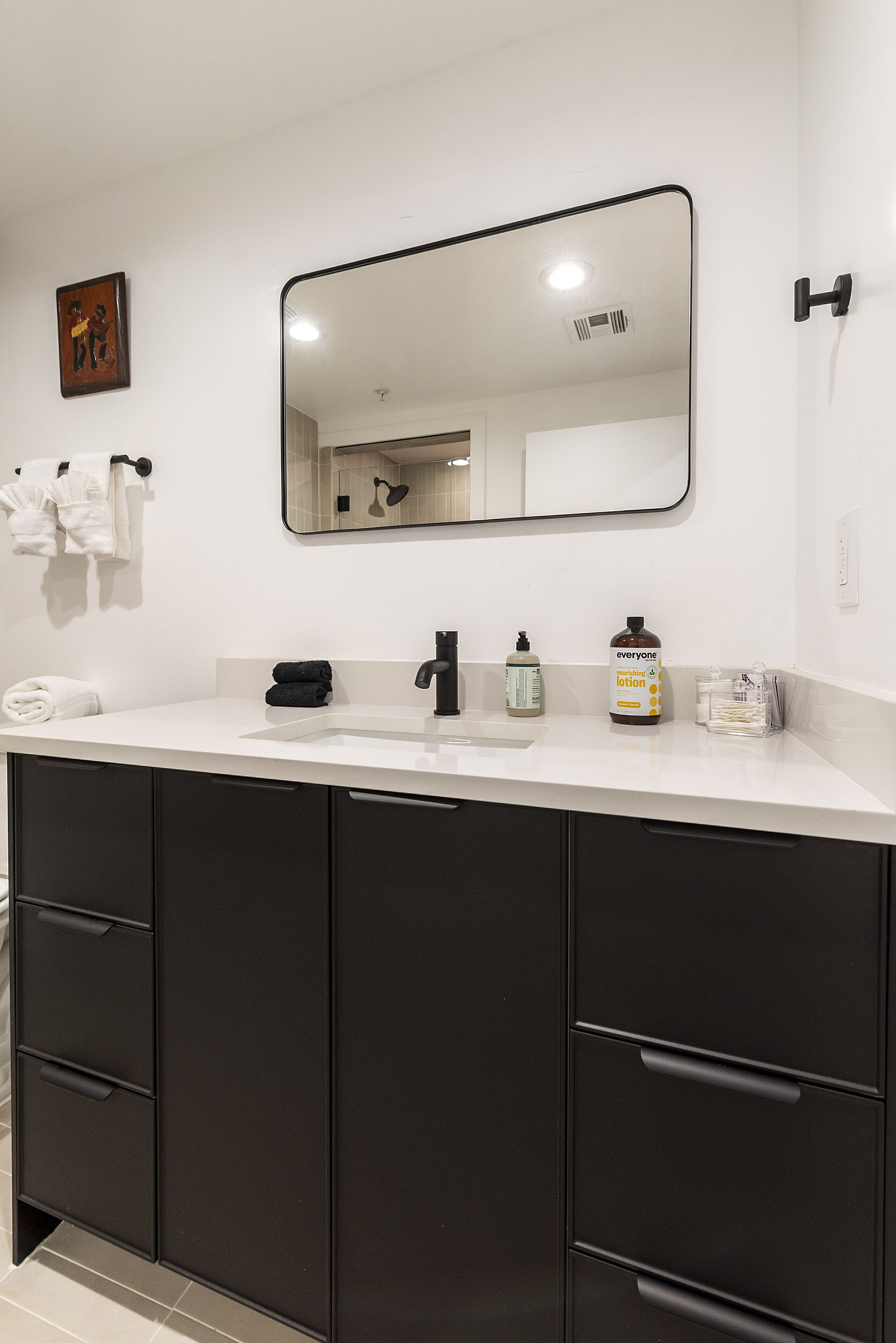 A modern bathroom with a white countertop, black cabinets, a large mirror, and toiletries.