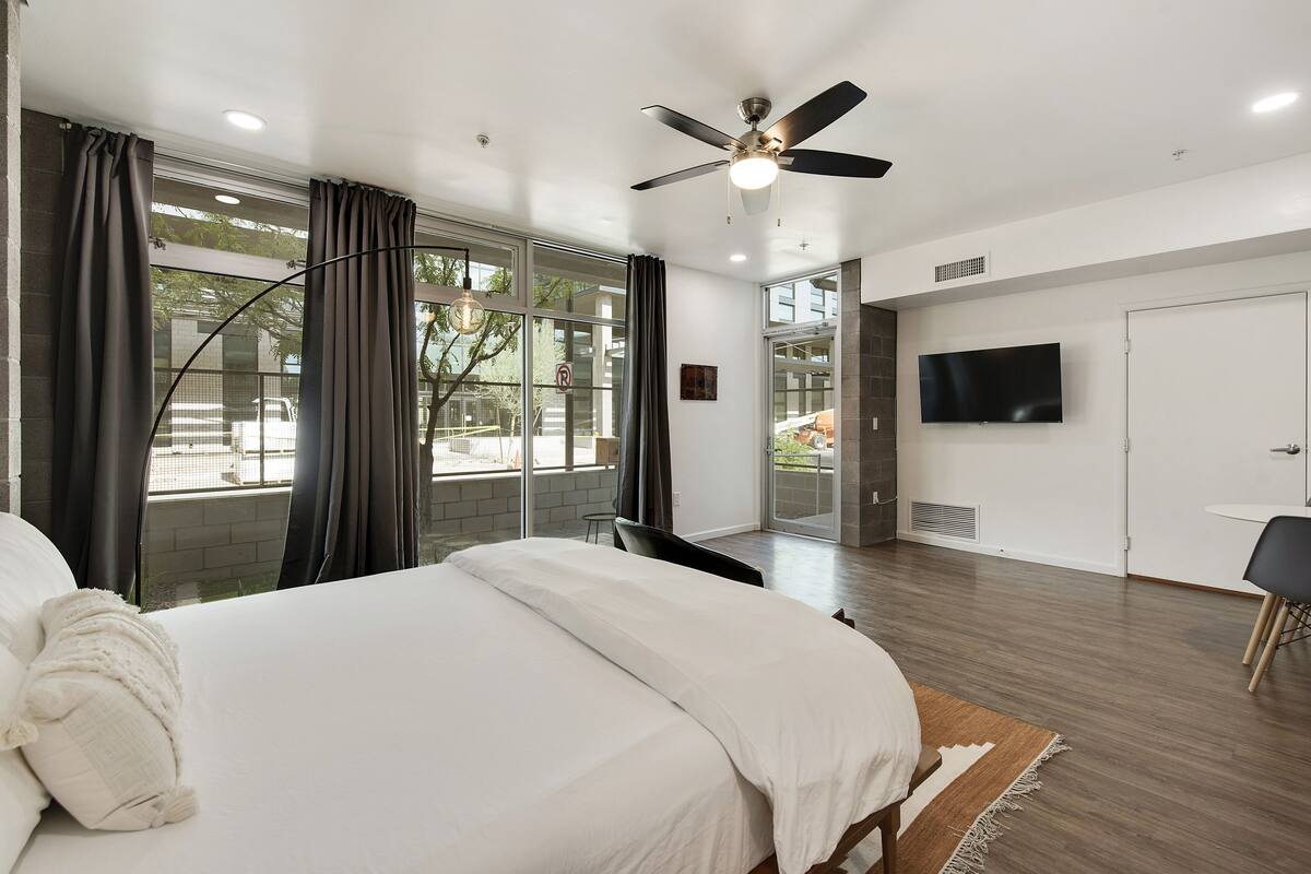 Habitación de hotel moderna con una cama grande, ventilador de techo, televisor de pantalla plana y balcón con vistas al exterior.