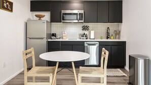 A modern kitchen with dark cabinets, a stainless steel microwave, a dishwasher, and a white dining table with wooden chairs. - Tempe Studios (Tempe)