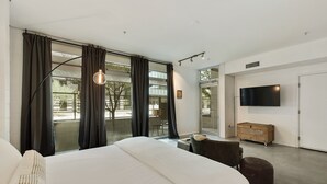 A modern bedroom with a large bed, a TV, and a view of the outdoors. - Tempe Studios (Tempe)