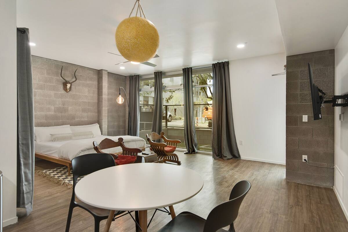 Una habitación de hotel moderna con una cama, una mesa redonda de comedor y un ventanal con cortinas.
