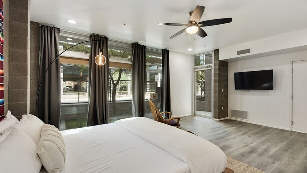 A modern bedroom with a large bed, a ceiling fan, a TV, and a view of the outdoors. - Tempe Studios (Tempe)