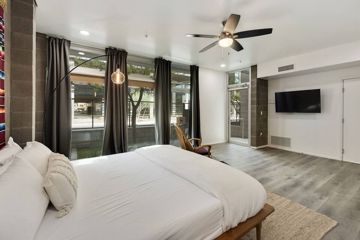 Un dormitorio moderno con una cama grande, ventilador de techo, televisor y vista al exterior.