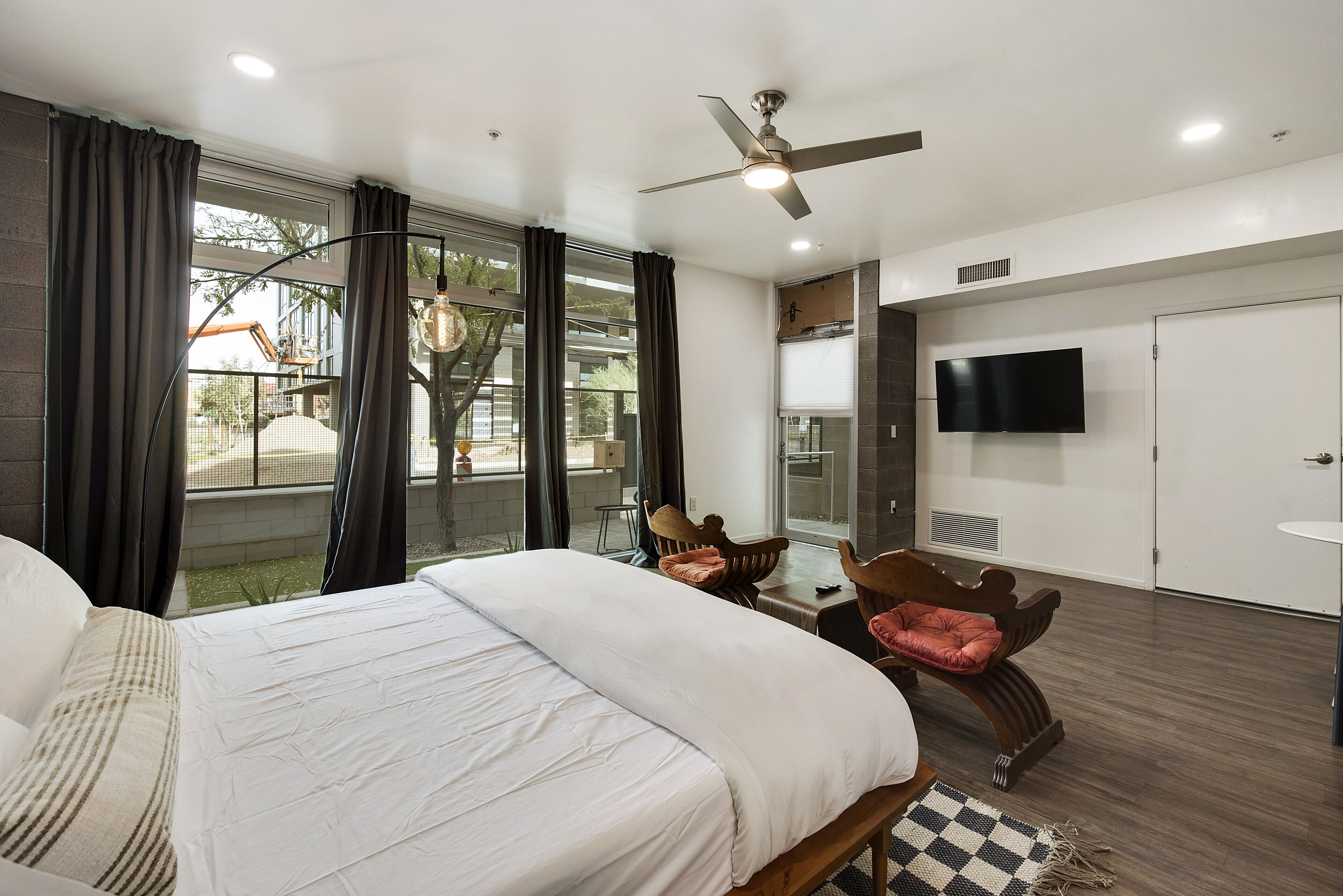 Quarto de hotel com uma cama grande, uma mesa, uma cadeira, uma televisão e uma varanda com cortinas.
