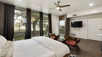 Quarto de hotel com uma cama grande, uma mesa, uma cadeira, uma televisão e uma varanda com cortinas.