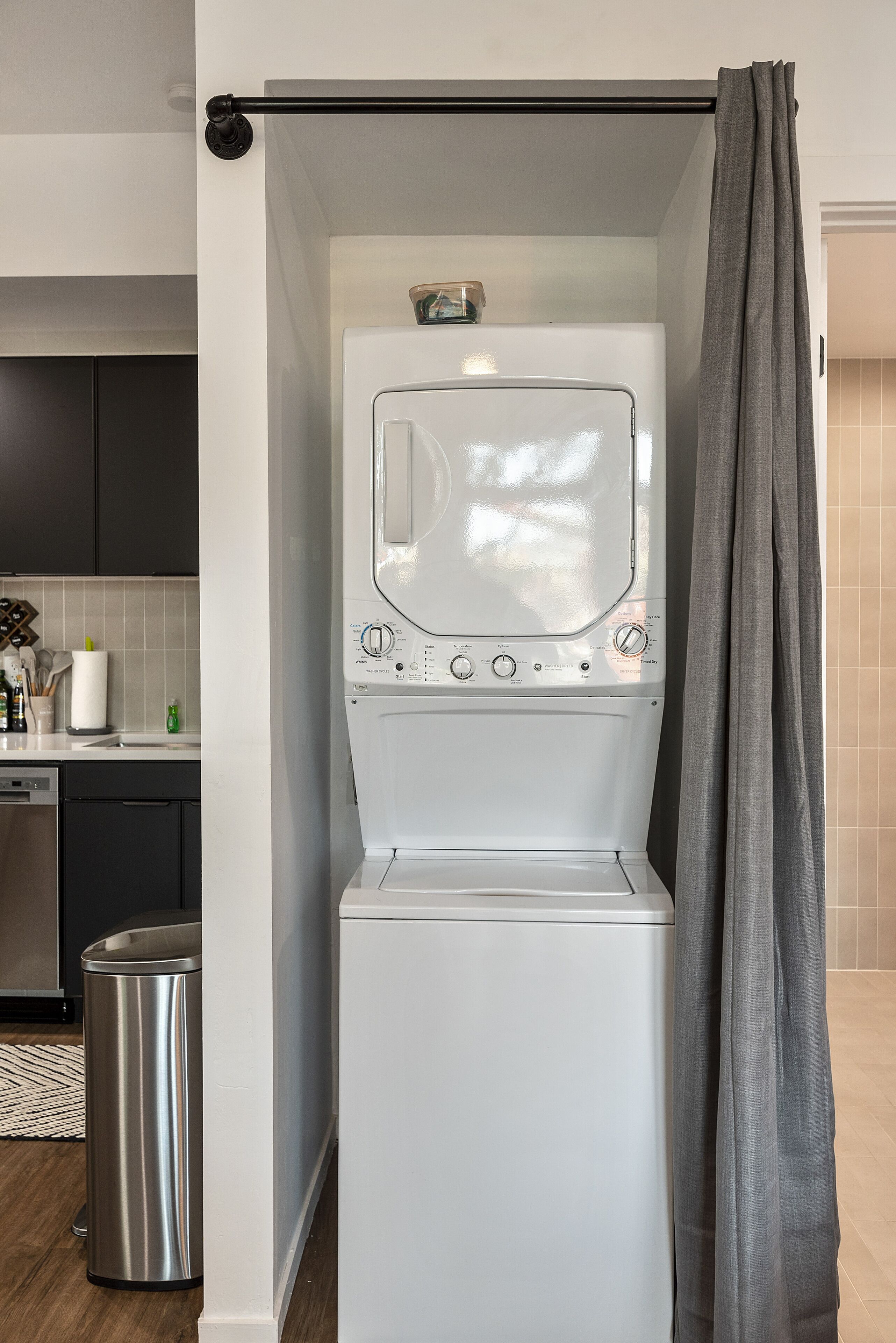 A compact laundry area with a washing machine, a drying rack, and a trash bin.