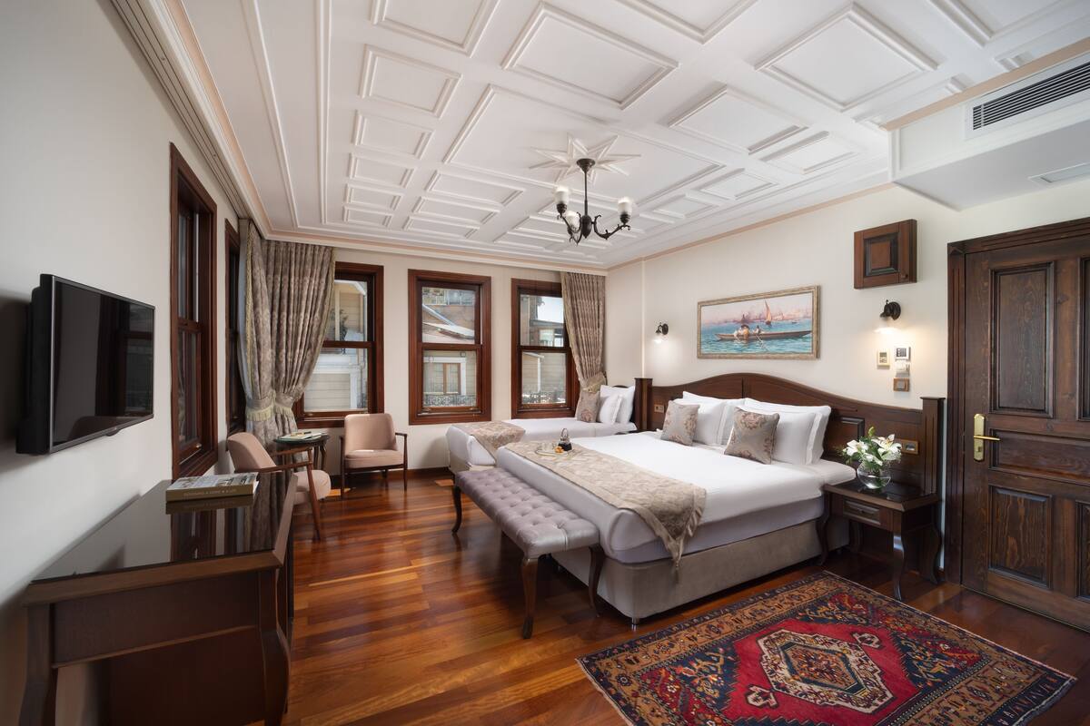 A spacious bedroom with a large bed, a television, a desk, and a bench.