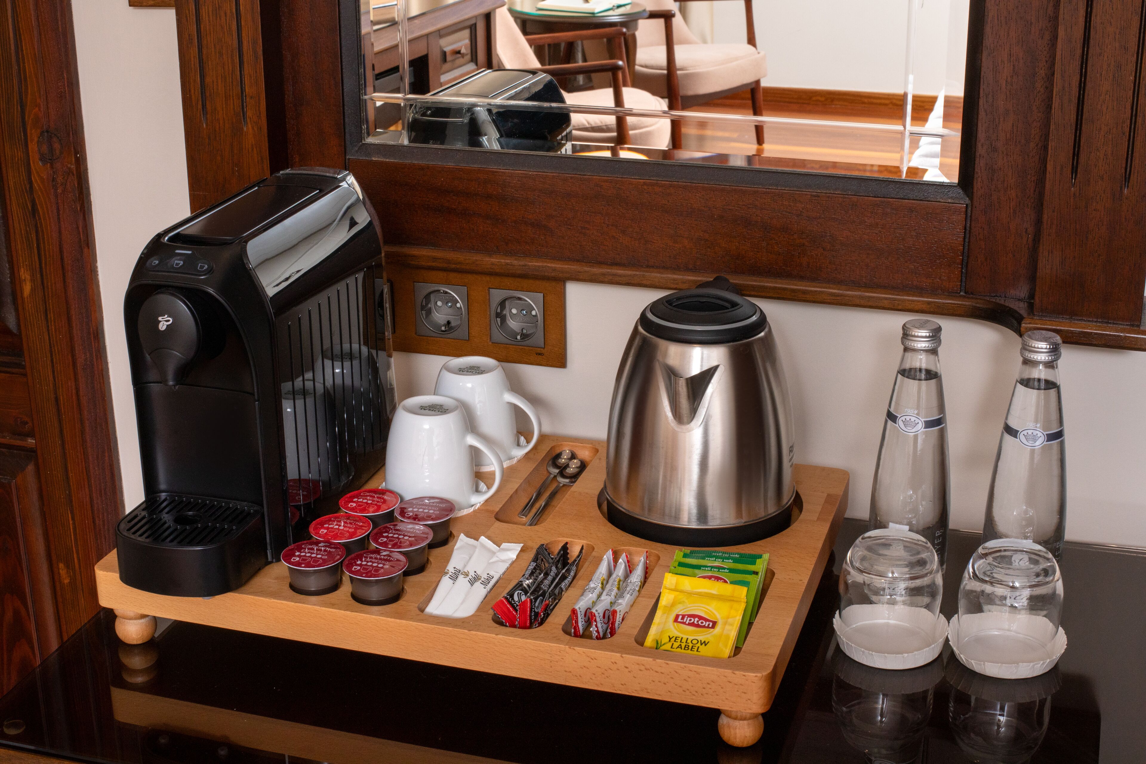 Een ontbijtarrangement met een koffiezetapparaat, kopjes, een waterkoker, toevoegingen en een dienblad.