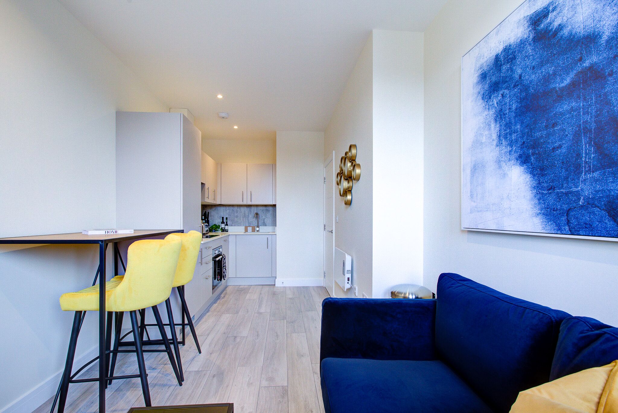Una cocina moderna con armarios blancos, una zona de comedor con sillas amarillas y un sofá azul.