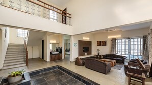 A spacious living area with a staircase leading to an upper floor, a kitchen in the background, and a seating area with sofas and a coffee table. - 4bhk Villa in Mulshi With Private Swimming Pool (Paud)