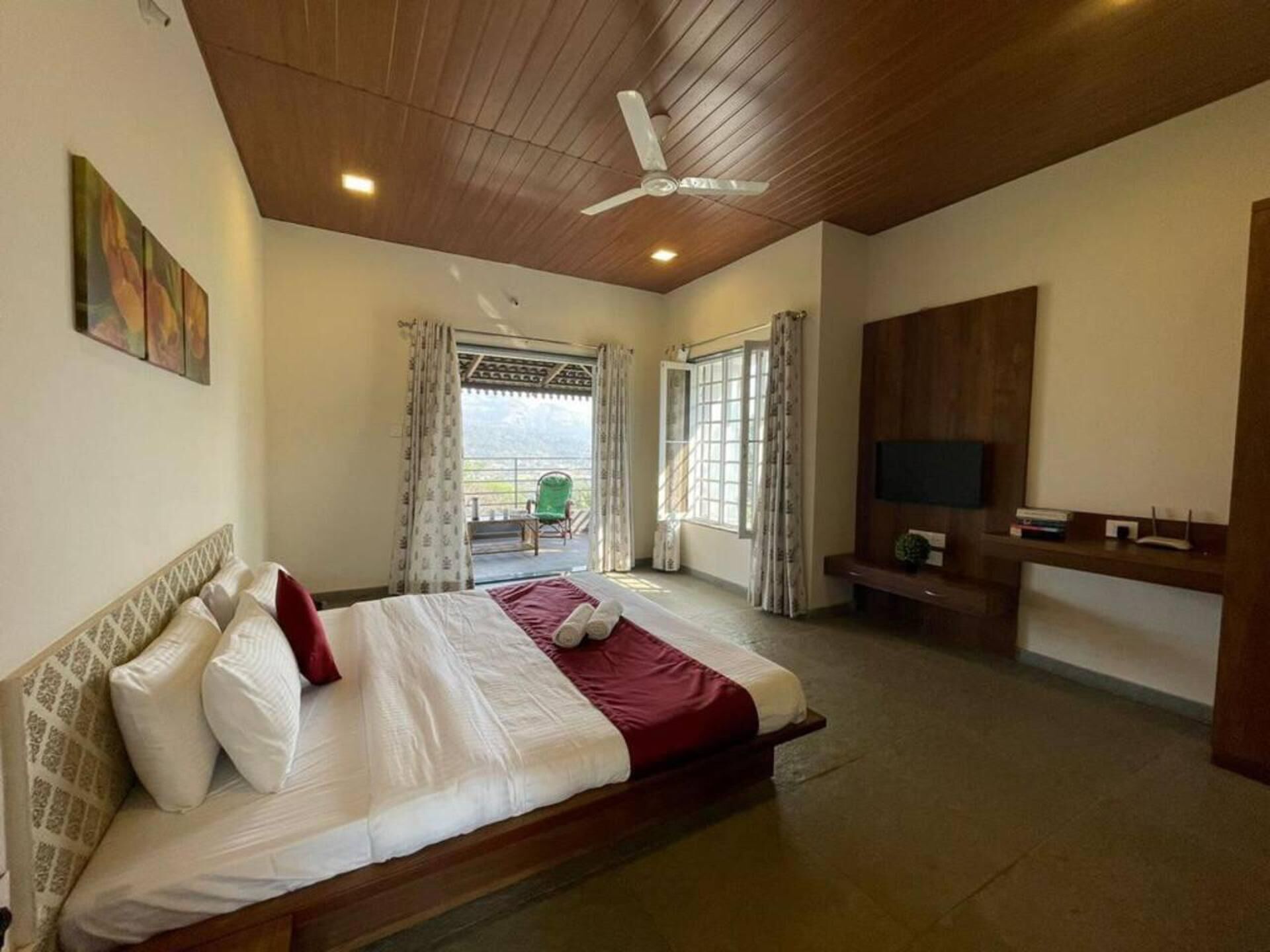 Ein Schlafzimmer mit Bett, Deckenventilator, Fernseher und Balkon mit einem Sessel.