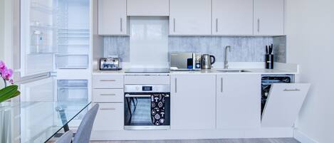 A modern kitchen with white cabinets, a built-in oven, a microwave, and a glass dining table.