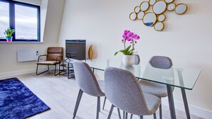 A modern dining area with a glass table, grey chairs, a blue rug, a potted orchid, and a decorative mirror wall. - Charming 2-bed Apartment in Cheam, Sutton (Sutton)