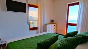 Ein Schlafzimmer mit einem Bett, zwei Fenstern mit Meerblick, einem Nachttisch und einem Sessel.